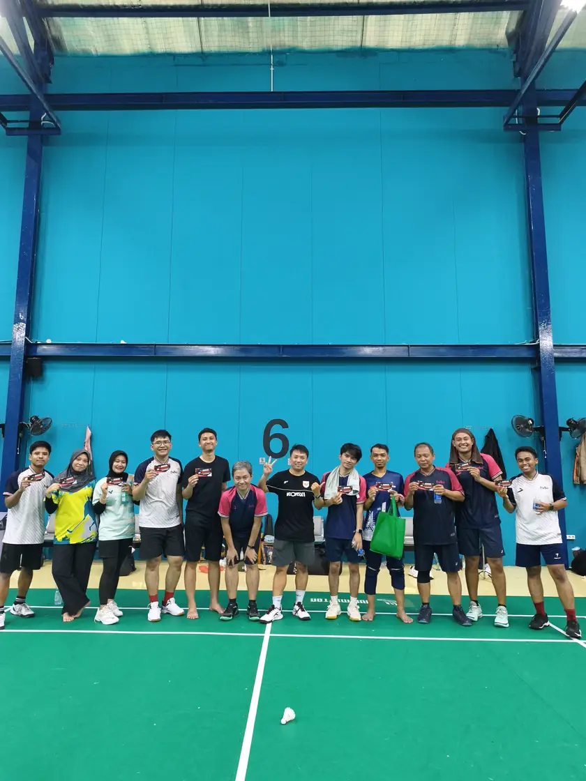 Anggota komunitas berfoto bersama setelah turnamen internal Fokbad dengan latar dinding lapangan biru.