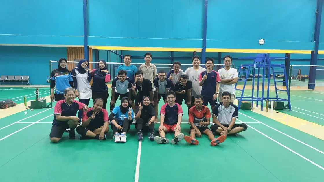 Anggota komunitas badminton berpose bersama di depan net seusai bermain.